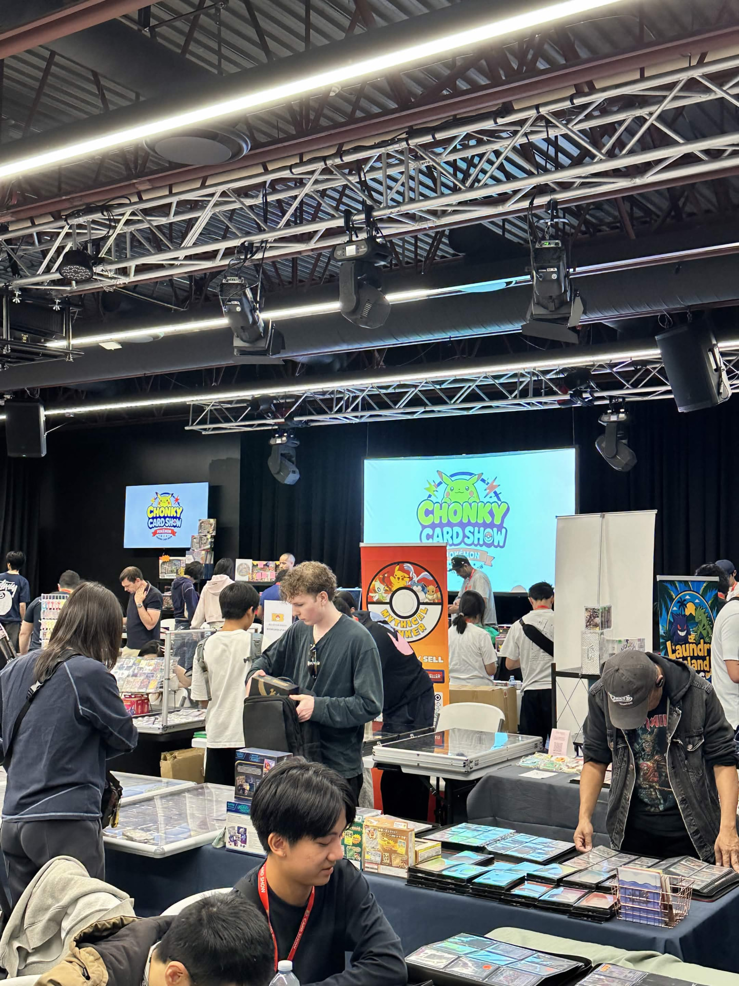 Attendees examining binders and display cases with the show screen behind